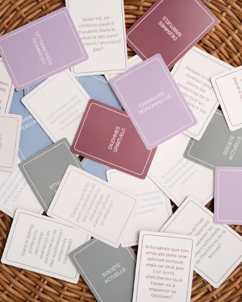Des cartes du jeu étalées dans un panier, questions visibles et catégories au dos.